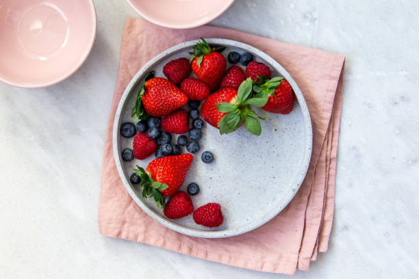 istock Mixed berries in conrete plate on marble background with empty plate and copy space 1130544758