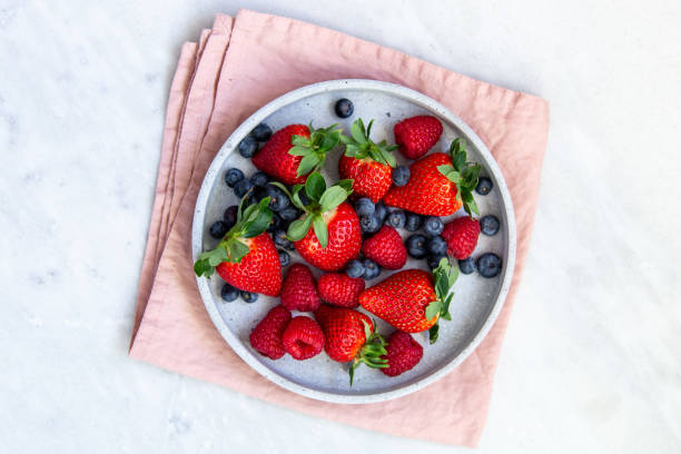 istock Mixed berries in conrete plate on marble background with empty plate and copy space 1130544890
