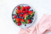 Mixed berries in conrete plate on marble background with empty plate and copy space