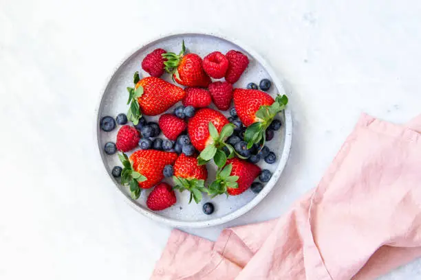 Photo of Mixed berries in conrete plate on marble background with empty plate and copy space