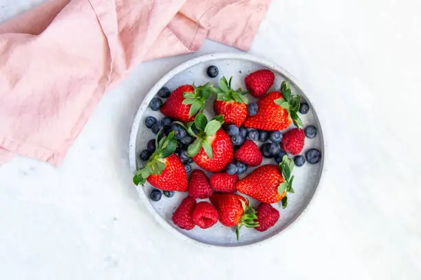 Photo of Mixed berries in conrete plate on marble background with empty plate and copy space