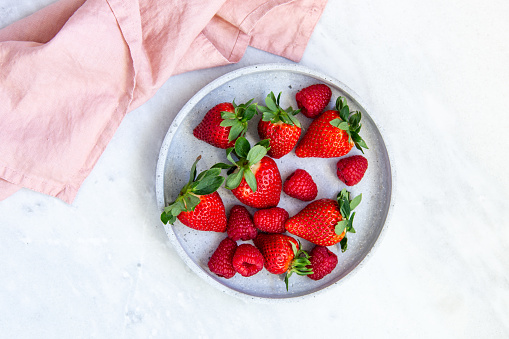 Summer healthy fruit composition with red strawberries and raspberries on marble background