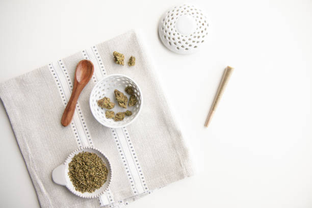 Marijuana Product Laid Out on Clean Place Mat and White Background. Buds, Joint, Flower, Ground Cannabis, Wooden Spoon, Bowl - Minimalist Cannabis stock photo