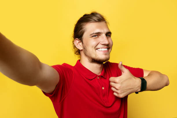 istock Happy-looking young man showing thumb up gesture while taking selfie on yellow background. 1130545003