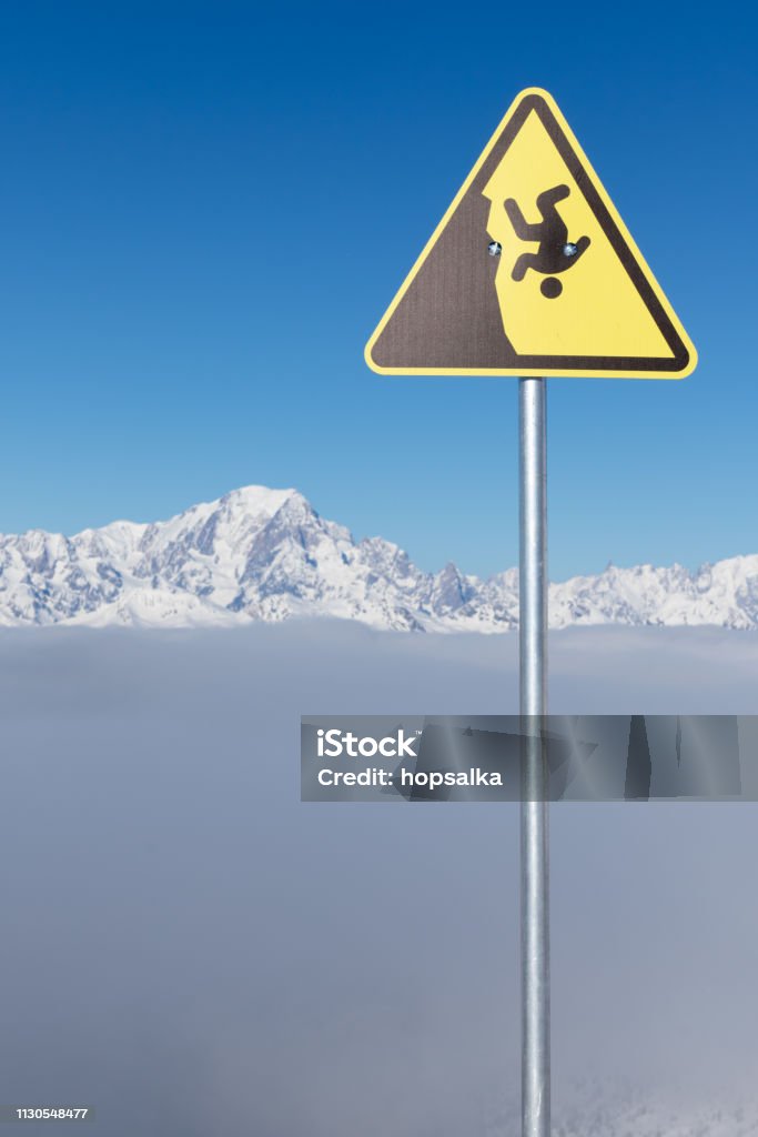 Yellow warning sign of possible fall from a cliff. Dangerous extreme sports concept. The highest European mountain Mont Blanc in background. Cliff Stock Photo