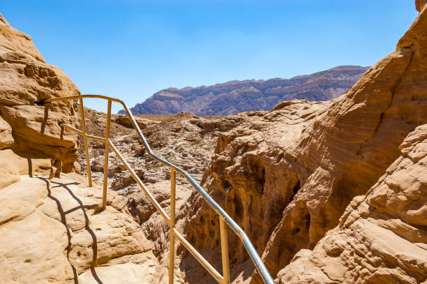 high trails secured by metal railings surrounded by caves, rocks, cliffs of ancient cooper mines canyons and mountains range in timna national park - ravine geology danger footpath imagens e fotografias de stock