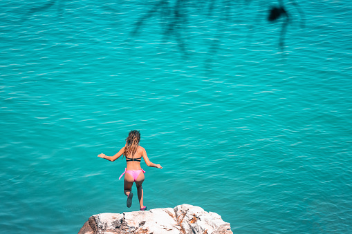 Young woman enjoying on summer vacations in Greece. She jumping from cliff and diving into blue sea