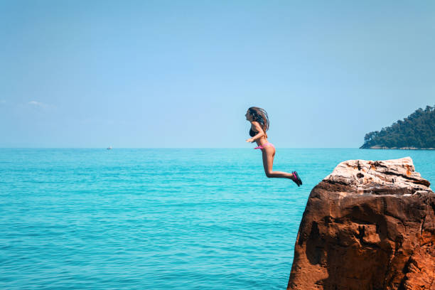 mujer joven en vacaciones de verano saltando desde el acantilado y el buceo en el mar azul - salto desde acantilado fotografías e imágenes de stock
