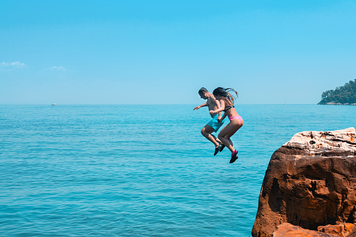 Father and daughter enjoying on summer vacations in Greece. They jumping together from cliff and diving into blue sea
