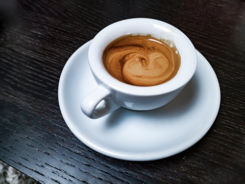 Small cup of espresso coffee on black table. The cup shape is typical for Naples, Italy.