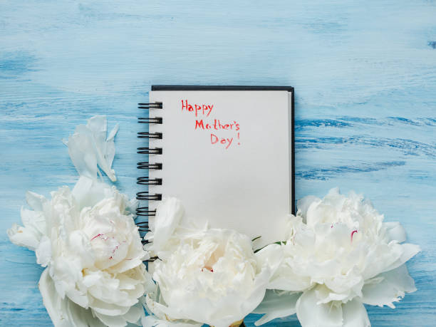 Bright flowers, notebook with congratulations on Mother's Day Bright flowers and notebook with congratulations on Mother's Day. Top view, close-up. Blue background. Happy family concept mothers day horizontal close up flower head stock pictures, royalty-free photos & images