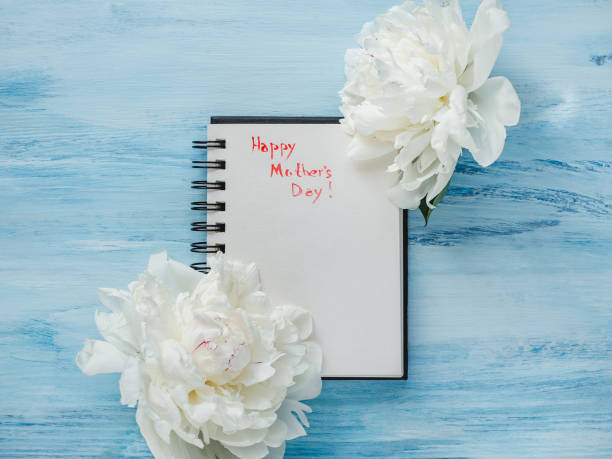 Bright flowers, notebook with congratulations on Mother's Day Bright flowers and notebook with congratulations on Mother's Day. Top view, close-up. Blue background. Happy family concept mothers day horizontal close up flower head stock pictures, royalty-free photos & images