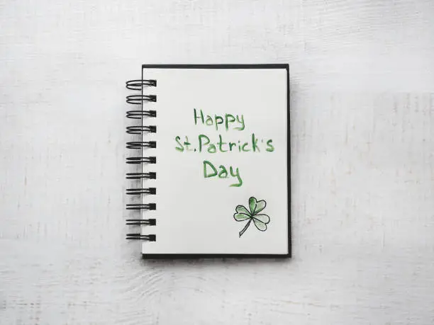 St.Patrick's Day. Beautiful card. Notebook with congratulatory inscription. Isolated background, wooden surface. Congratulations for loved ones, relatives, friends and colleagues