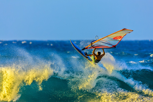 A child who learns to surf in the sea at a beautiful sunset, close-up, windsurfing lessons and school. With copy room.