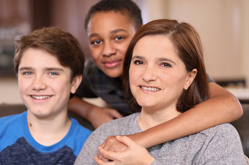 Multi-ethnic family members at home sharing a hug.  Single latin descent mother at right.  Adopted child center.