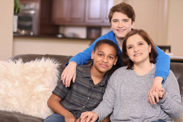 Multi-ethnic, adoption or foster care family at home. Multi-ethnic family members at home sharing a hug.  Single latin descent mother at right.  Adopted child at left. foster care stock pictures, royalty-free photos & images