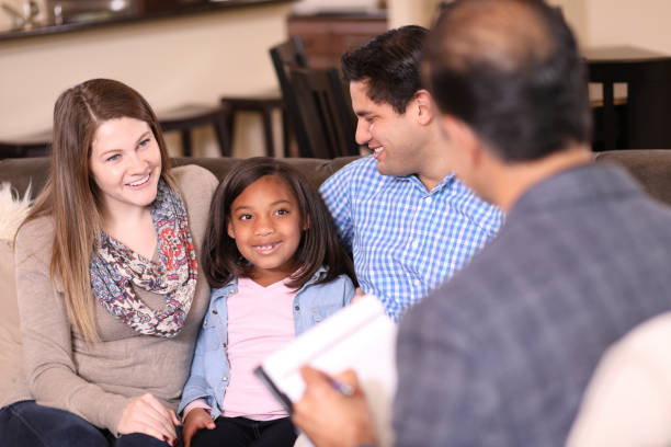 Family counseling session at home with therapist. Multi-ethnic family at home with mental health professional, social worker, or family therapist.  Adopted child with young family. foster care stock pictures, royalty-free photos & images