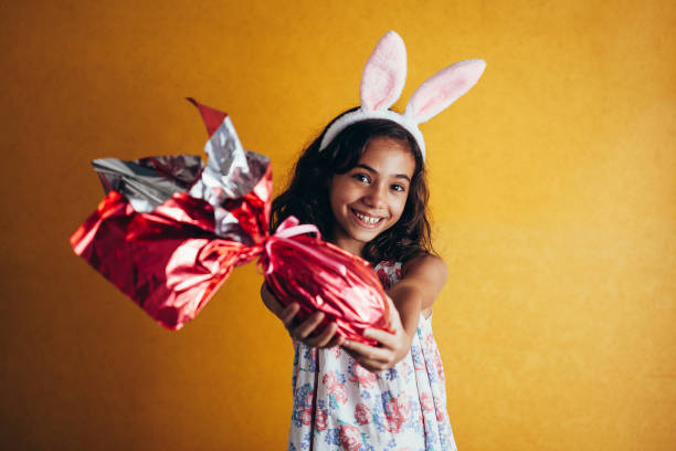 niedliche kleine kind trägt hasenohren am ostersonntag auf farbigem hintergrund. mädchen halten schokoladen-osterei - easter easter egg child chocolate stock-fotos und bilder