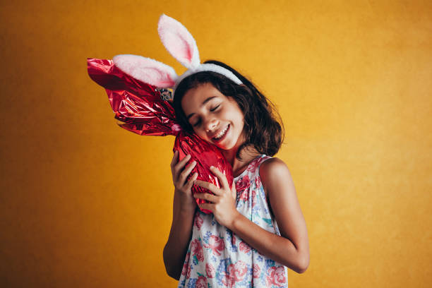 симпатичный маленький ребенок носить кролика уши на пасху день на цветном фоне. девушка, держащая шоколадное пасхальное яйцо - child easter flower little girls стоковые фото и изображения
