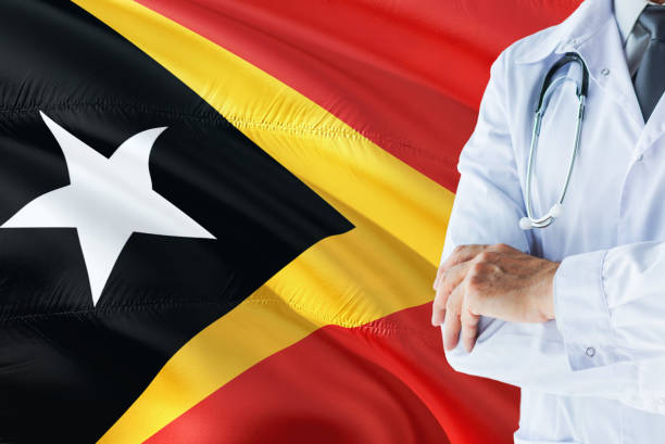 Timorese Doctor standing with stethoscope on East Timor flag background. National healthcare system concept, medical theme. timorenses médico con estetoscopio sobre fondo de bandera de timor oriental. concepto de sistema nacional de salud, tema médico. timorenses médico con estetoscopio sobre fondo de bandera de timor oriental. concepto de sistema nacional de salud, tema mé