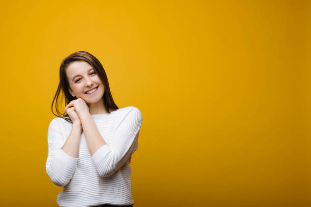 istock Kind young girl looking smiling into camera leaning her head on her hands against yellow background. 1130573948
