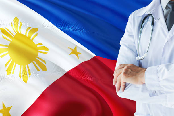 filipino médico permanente com estetoscópio sobre fundo de bandeira de filipinas. conceito de sistema nacional de saúde, tema médico. filipino médico permanente com estetoscópio sobre fundo de bandeira de filipinas. conceito de sistema nacional de sa - philippino flag - fotografias e filmes do acervo