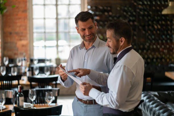 istock Cheerful manager and waiter talking about the booking arrangements while waiter points at a document both smiling 1130576068