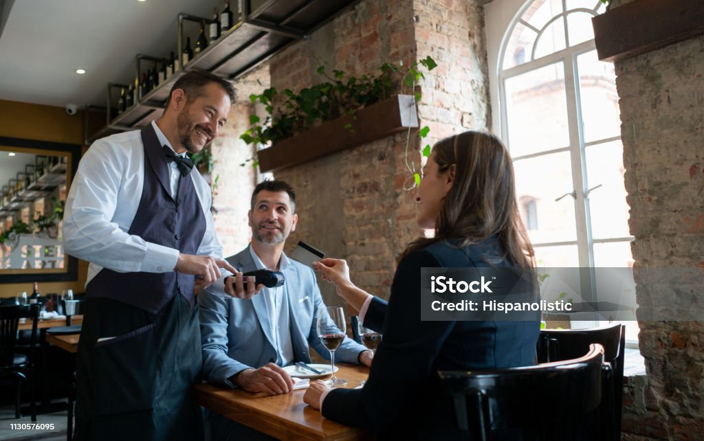 Latin american adult couple at a restauyrant on a date and woman paying with a credit card to waiter Latin american adult couple at a restauyrant on a date and woman paying with a credit card to waiter all smiling Restaurant Stock Photo