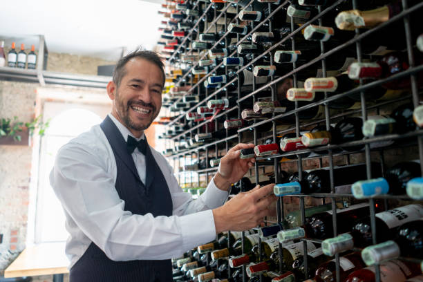 sommelier masculin dans un restaurant saisissant des bouteilles de vin du rack tout en faisant face au sourire de caméra - winetasting wine wine rack bar counter photos et images de collection