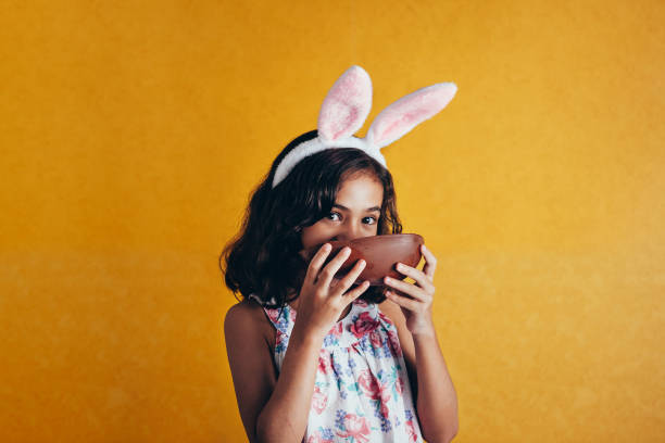 색상 배경에 부활절 날에 토끼 귀를 입고 귀여운 작은 아이. 여자 먹는 초콜릿 부활절 달걀 - easter easter egg child chocolate 뉴스 사진 이미지