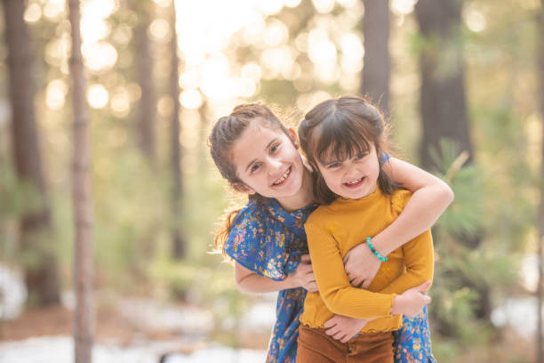 Two happy sisters taking a break from a play while sitting in autumn leaves in the forest