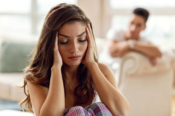 Just calm down and take a deep breath! Frustrated woman holding her head in pain and trying to calm down after the conflict she had with her boyfriend. The man is sitting in the background. woman mascara smudged stock pictures, royalty-free photos & images