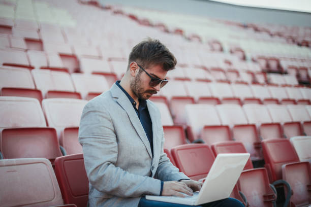 istock Businessman using laptop at the stadium and watching the game 1130595735