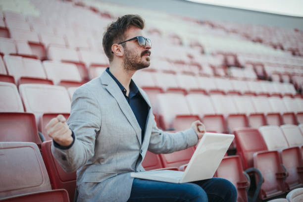 istock Businessman using laptop at the stadium and watching the game 1130595758