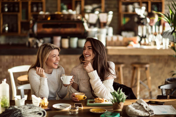 Two cheerful women having fun during coffee time in a cafe. Young happy women talking and laughing while drinking coffee together in coffee shop. drinking coffee drink stock pictures, royalty-free photos & images