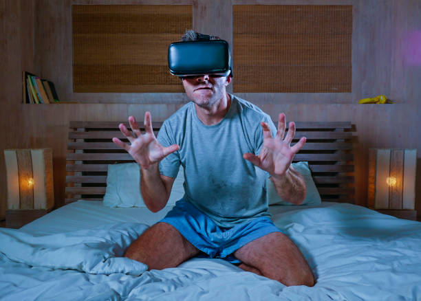 young excited and aroused man at home wearing 3d virtual realty goggles having fun on bed playing alone with internet cyber sex VR simulator in sexual illusion and desire concept stock photo