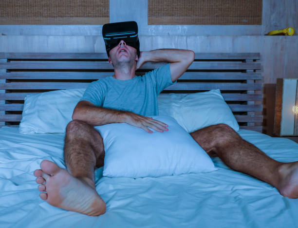 young excited and aroused man at home wearing 3d virtual realty goggles having fun on bed playing alone with internet cyber sex VR simulator in sexual illusion and desire concept stock photo