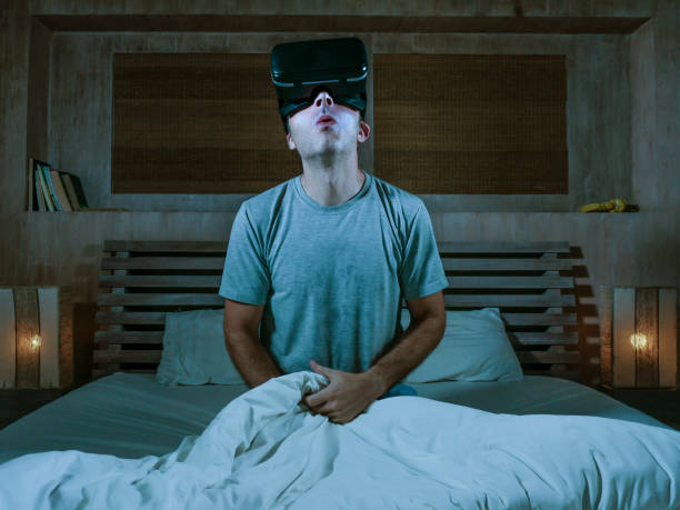 young excited and aroused man at home wearing 3d virtual realty goggles having fun on bed playing alone with internet cyber sex VR simulator masturbating in sexual illusion and desire stock photo