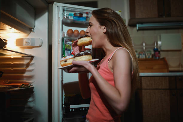 istock Young woman eating doughnuts in the kitchen late night 1130604808