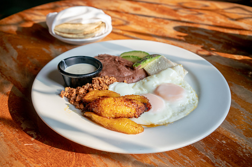 Honduras breakfast with fried plantains, eggs, beans, chorizo, crema and corn tortillas