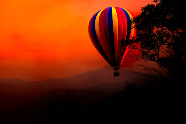 Hot air balloon float on the sky at sunset. Background and foreground are mountain and tree.