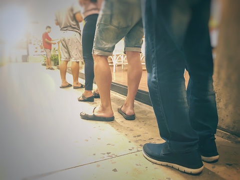 Row of People in queue for waiting something. Back of man and woman orderly in line. Close up legs of people