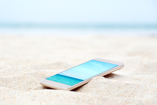 Modern smart phone on the beach with travel photo. Vacation background.