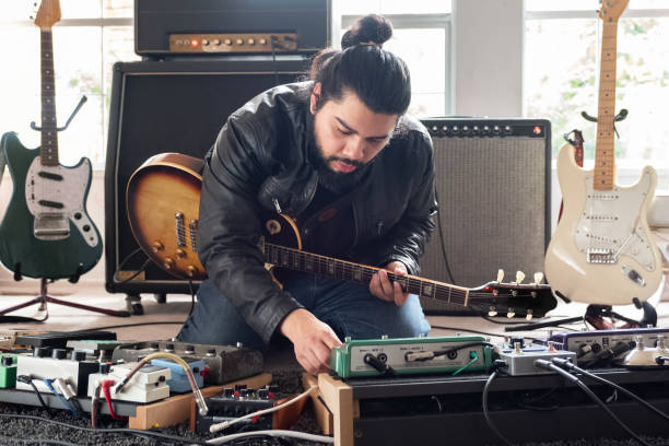 guitarrista masculino rodeado de equipos de sonido ajustando los pedales de efectos de sonido - equipo musical fotografías e imágenes de stock