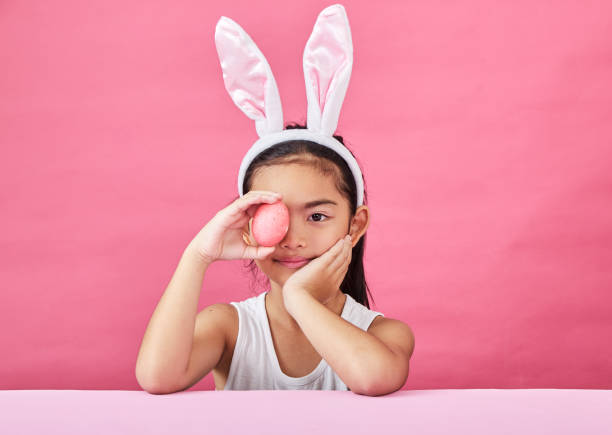 istock Little girl in a rabbit costume with Easter eggs on a pink background. 1130638120