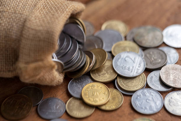 Coins Spilling Out From Sack Indian coins spilling out from a burlap sack on a wooden surface. Indian currency background concept. buying gold for retirement stock pictures, royalty-free photos & images
