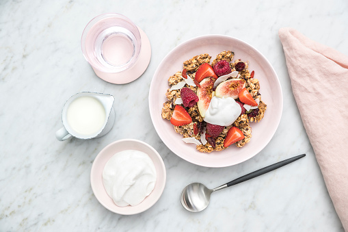 Bowl of muesli/granola clusters topped with fresh fruit and a side of yoghurt and milk
