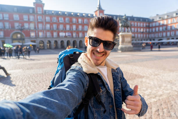 istock Attractive young tourist student man with backpack having fun happy and excited taking a funny face selfie with smart phone in Plaza Mayor, Madrid, Spain. Vacation, and travel around the world concept. 1130641594