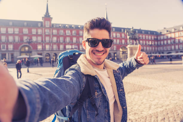 istock Attractive young tourist student man with backpack having fun happy and excited taking a smiling face selfie with smart phone in Plaza Mayor, Madrid, Spain. Vacation, and travel around the world concept. 1130641596