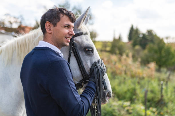 Man horseback rider standing close to white horse, stroking its head